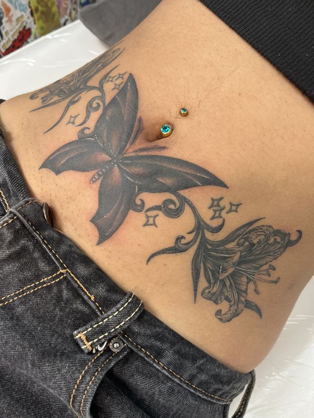 Large black and grey butterfly with stars and lilies across the stomach and hip.