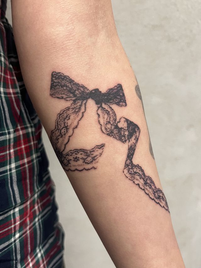 Fine line lace ribbon tied in a bow, trailing down a forearm.